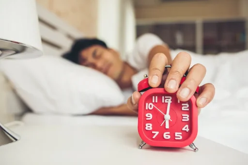 Man waking up to an alarm clock, representing overcoming laziness