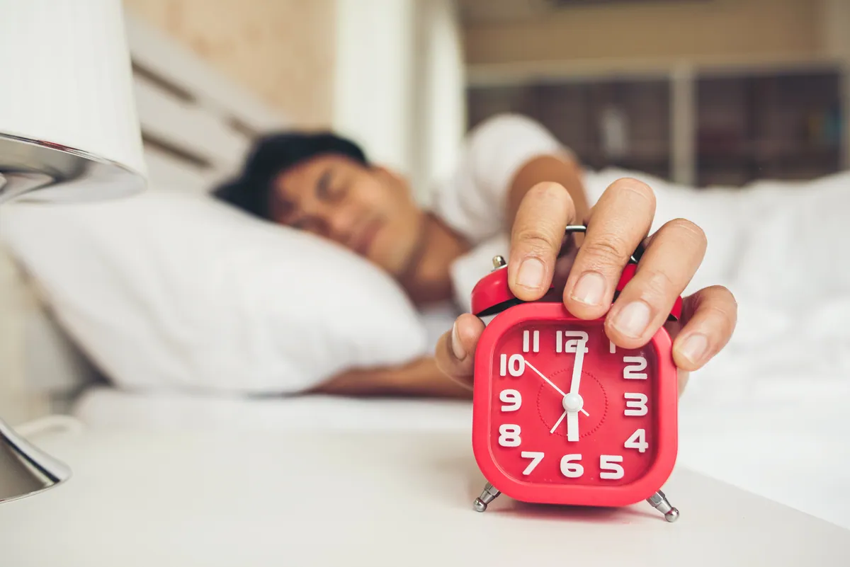 Man waking up to an alarm clock, representing overcoming laziness